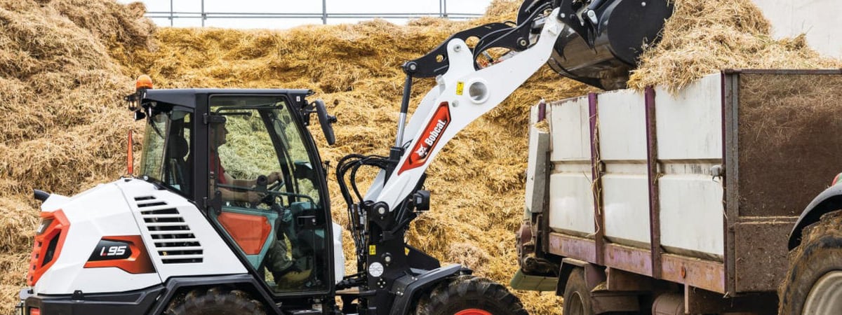 Bobcat loader filling a truck with hay